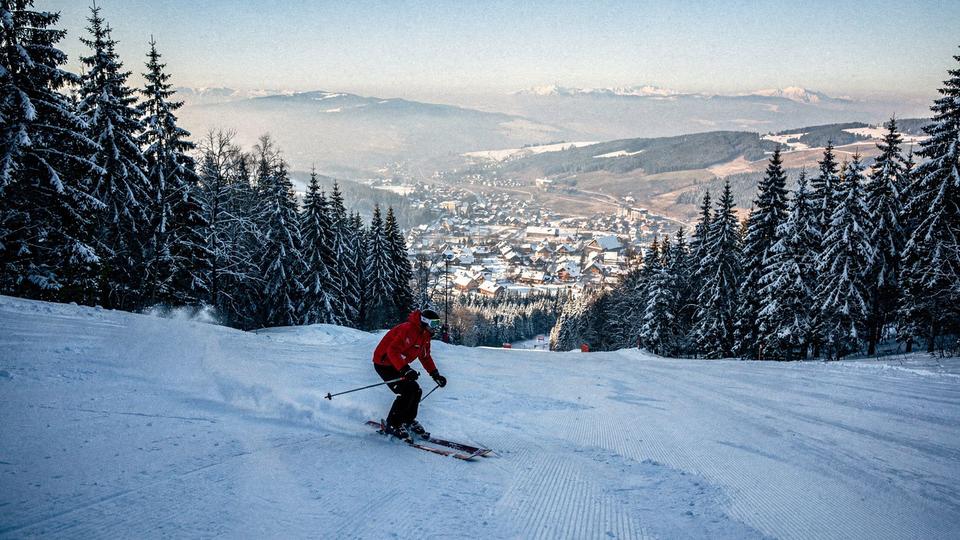 Skier on a groomed slope above a Carpathian resort village in mid February